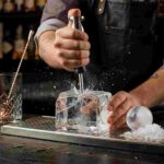 Bartender Using Heavy Duty Stainless Steel Ice Pick to Break Ice Blocks in Professional Craft Bar