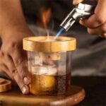 Bartender Using Mixology Wood Smoker for Table-Side Smoke Infusion in Luxury Bar