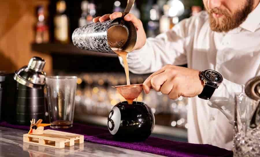 cocktail strainer in use pouring drink through hawthorne strainer into glass bar