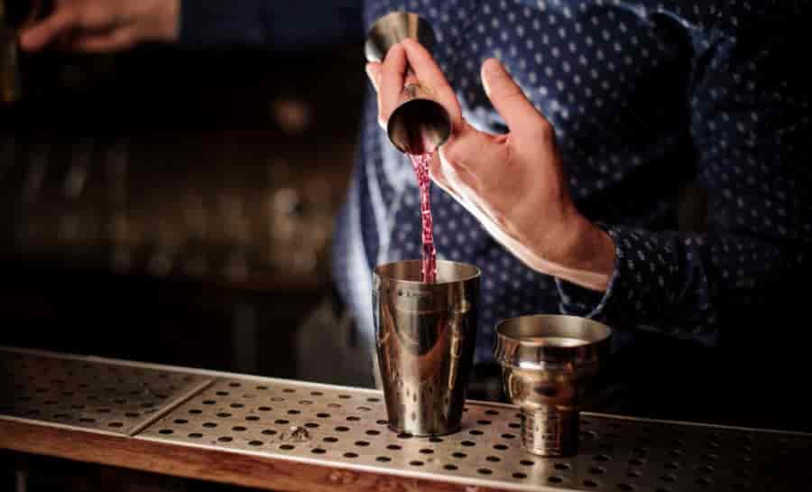 professional bartender using stainless steel jigger to measure cocktail ingredients at bar