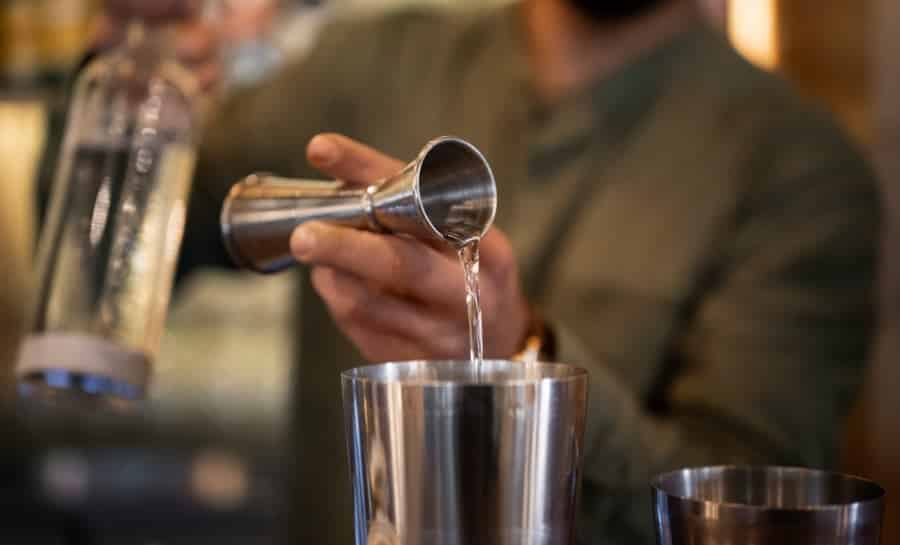 bartender using cocktail jigger to measure spirits stainless steel bar tool professional